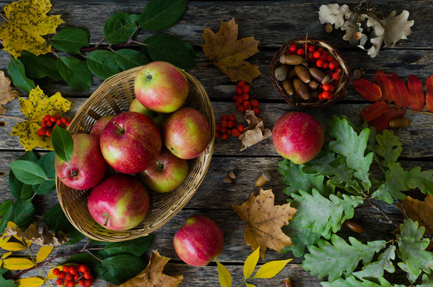 Apples in wicker basket on a background of autumn leaves and old boards - Photo, image