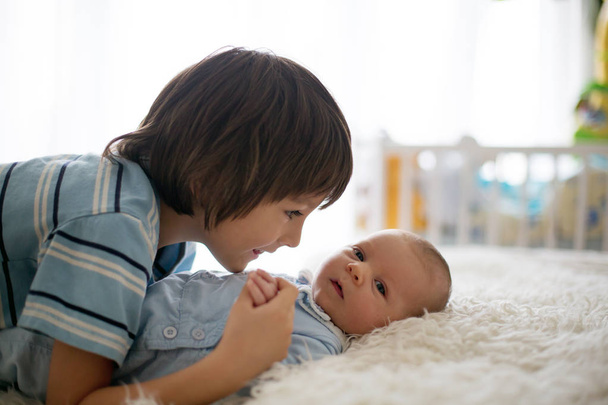 schöner Junge, umarmt mit Zärtlichkeit sein neugeborenes Baby - Foto, Bild