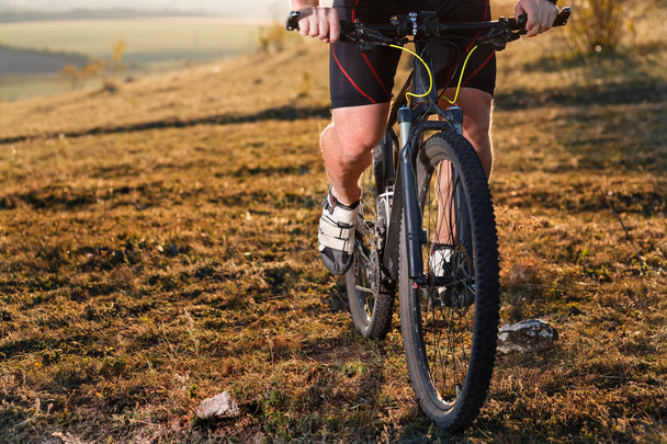 Крупный план человека-велосипедиста ноги и руки верхом на горном велосипеде на открытой тропе в природе
 - Фото, изображение