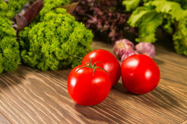 Fresh ripe tomatoes on a wooden table with a green salad on the background. Fresh vegetables. Delicious vegetarian food. Salad. - Φωτογραφία, εικόνα