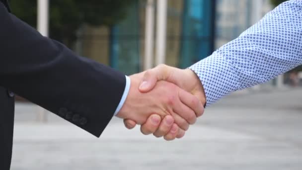 Two businessmen greeting each other in urban environment. Business handshake outdoor. Shaking of male arms outside. Colleagues meet and shake hands in the city background. Close up Slow motion - Footage, Video