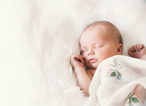 Sleeping newborn baby in a wrap on white blanket. - Zdjęcie, obraz