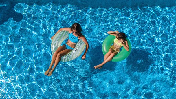 Aerial top view of children in swimming pool from above, happy kids swim on inflatable ring donuts and have fun in water on family vacation - Photo, Image
