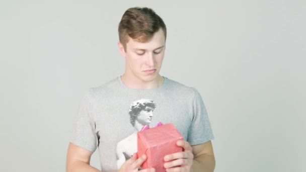 young man looks at the gift and wants to know whats inside on white background - Кадры, видео