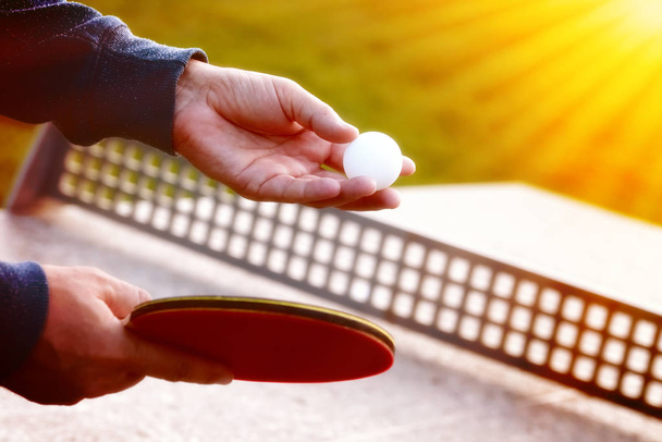 Nahaufnahme der Hände eines Tennisspielers mit Tennisschläger vor dem Hintergrund der Natur bei sonnigem Tag.Nahaufnahme eines Mannes, der im Tischtennis dient. Tischtennis im Freien - Foto, Bild