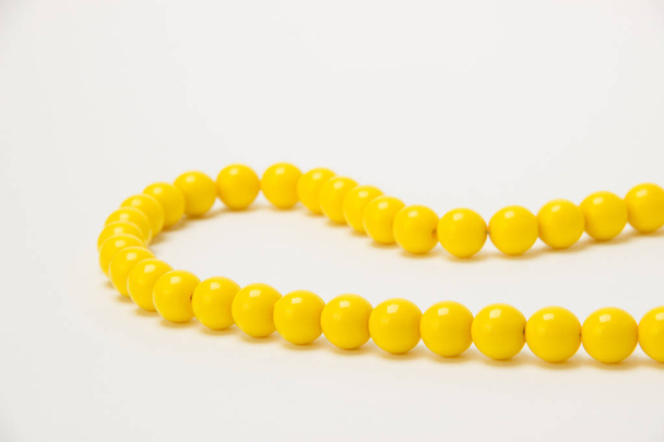 Necklace of yellow beads with green flowers on a white backgroun - Fotó, kép