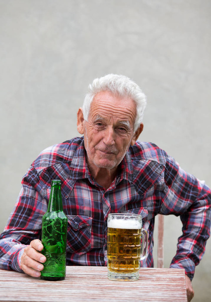 Senior man met bierfles en mok - Foto, afbeelding