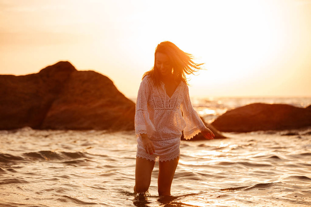 Joyful brunette woman in light summer dress walking in sea - Zdjęcie, obraz