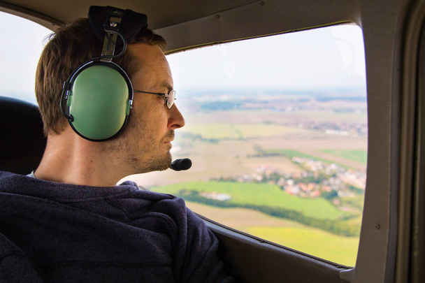Retrato de un pasajero adulto joven sentado en un avión privado y mirando por la ventana
 - Foto, Imagen