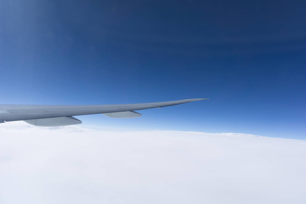 Lentokoneen siipi pilven yläpuolella kirkkaan sinisen taivaan alla
. - Valokuva, kuva
