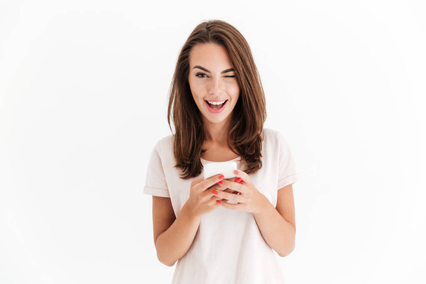 Happy brunette woman holding smartphone and winks at the camera - Foto, imagen