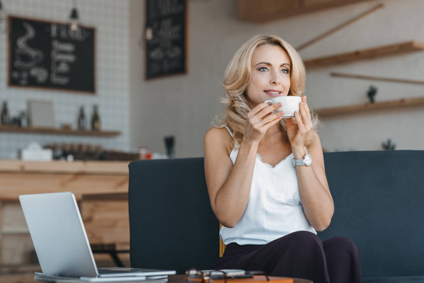 Nainen juo kahvia ja käyttää kannettavaa
 - Valokuva, kuva