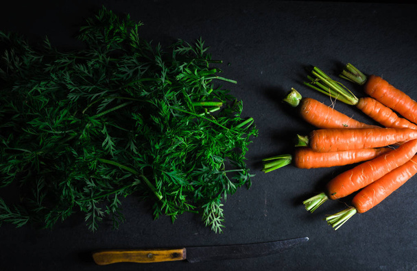 Carrots, sliced tops and a knife on a gray stone - 写真・画像