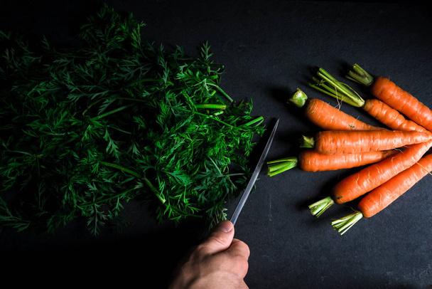Sliced tops of carrots, carrots and and a knife in hand - Foto, Imagen