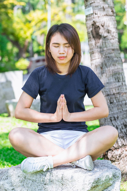 Aziatische tiener zittend ontspannen yoga concentratie met handen samen voor gezond in het park - Foto, afbeelding