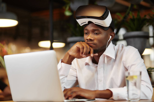 Serious african man i virtual head set, using laptop. - Foto, imagen