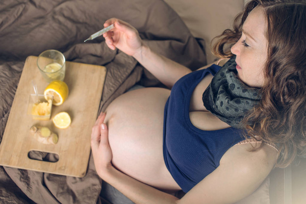 Mujer embarazada acostada en la cama enferma de resfriados y gripe. Mujer tratada con té de jengibre limón y miel
. - Foto, Imagen