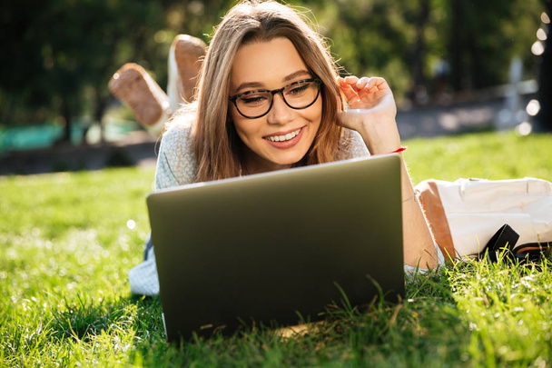 Happy brunette woman in eyeglasses lying on grass - Фото, зображення