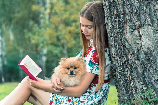 A girl is walking with a park with a dog. Pomeranian Spitz - Zdjęcie, obraz