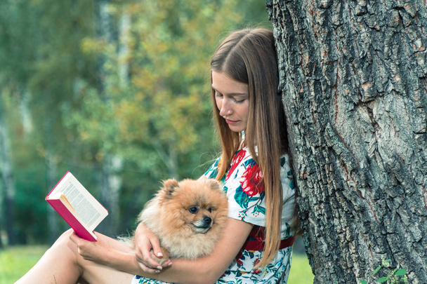 A girl is walking with a park with a dog. Pomeranian Spitz - Zdjęcie, obraz