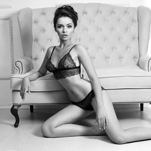 Woman in black lingerie set sitting on floor and leaning on sofa - 写真・画像