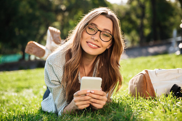 Pleased brunette woman in eyeglasses lying on grass - Foto, afbeelding
