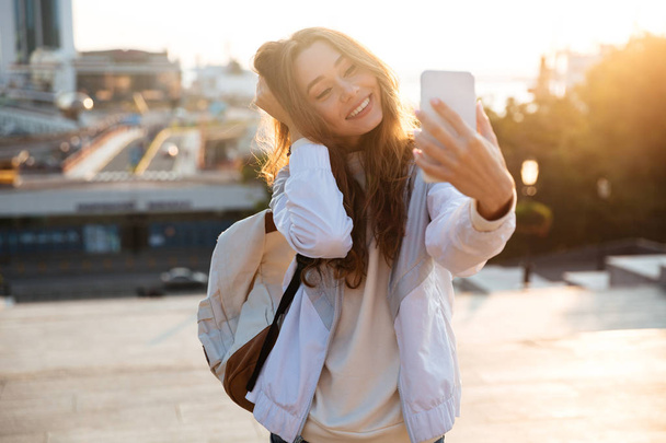 Mujer morena feliz en ropa de otoño haciendo selfie en el teléfono inteligente
 - Foto, Imagen