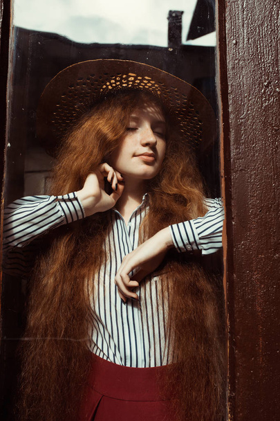 Krásnou mladou rusovláskou v slaměný klobouk za dřevěnými dveřmi - Fotografie, Obrázek
