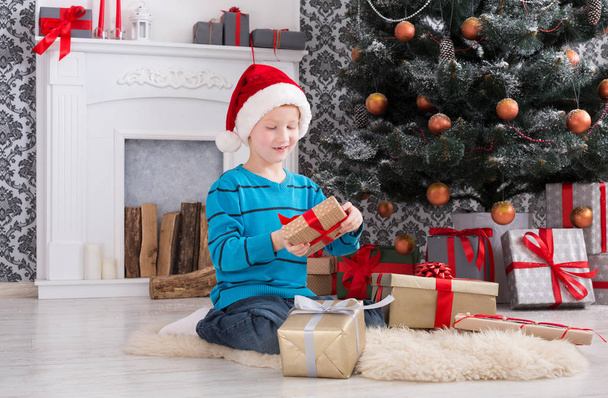 Cute boy in santa hat unwrapping christmas presents - Foto, imagen