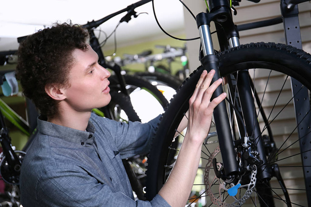 Young man choosing bicycle in shop - Foto, afbeelding