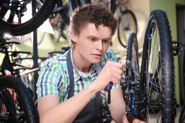 Young man checking bicycle in repair shop - Foto, afbeelding