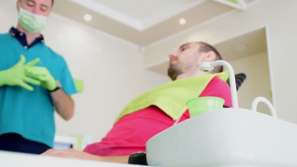 Young handsome man sitting on dental chair while his dentist fixes his teeths - Footage, Video