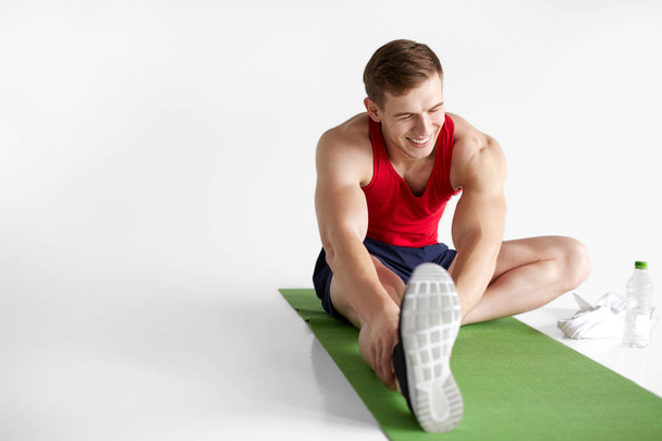 Smiling sportsman stretching on mat - Foto, imagen