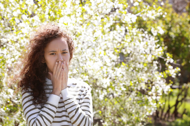 Allergy concept. Young woman suffering from cough among blooming trees in park - Foto, Bild