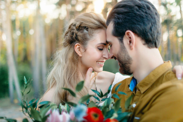 A young couple smile and touching foreheads. Autumn wedding ceremony outdoors. Bride and groom look at each other with tenderness and love. Close-up portrait - Foto, afbeelding