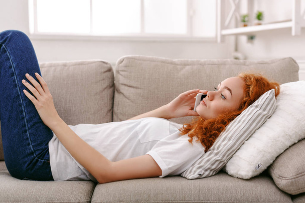 Fiatal lány beszél a mobil feküdt bézs kanapé - Fotó, kép