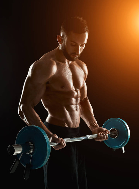 muskulöser Mann stemmt Gewichte vor dunklem Hintergrund - Foto, Bild