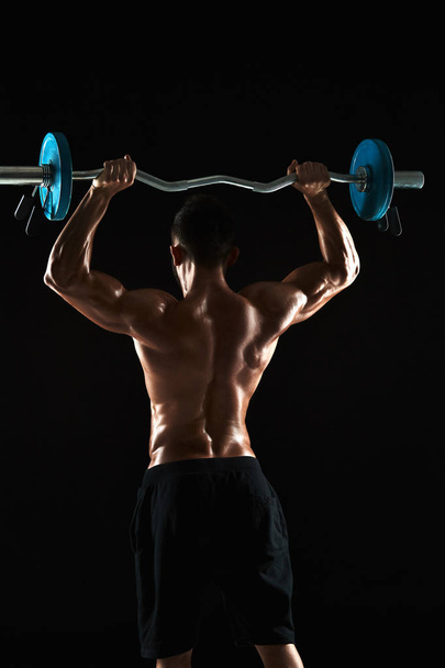 bodybuilder opheffing van een barbell op zwarte achtergrond - Foto, afbeelding