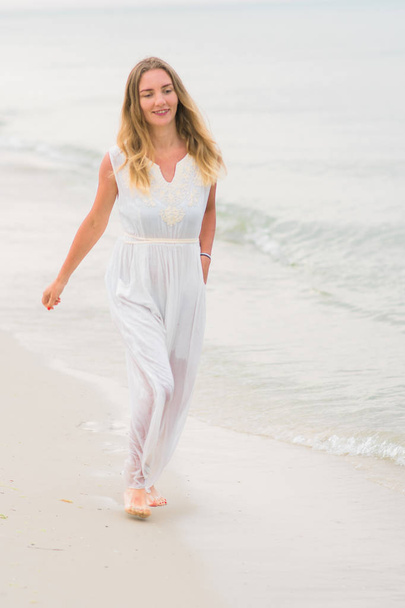 Lifestyle γυναίκα που τρέχει σε ένα λευκό φόρεμα στις ακτές του ωκεανού κάθετη εκτόξευση - Φωτογραφία, εικόνα