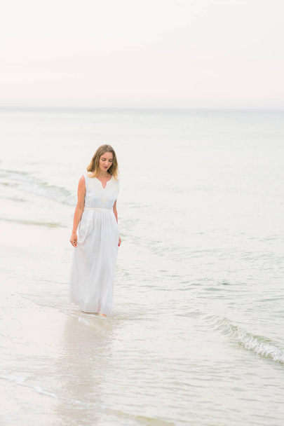 Lifestyle γυναίκα να στέκεται σε ένα λευκό φόρεμα στις ακτές του ωκεανού κάθετη εκτόξευση - Φωτογραφία, εικόνα