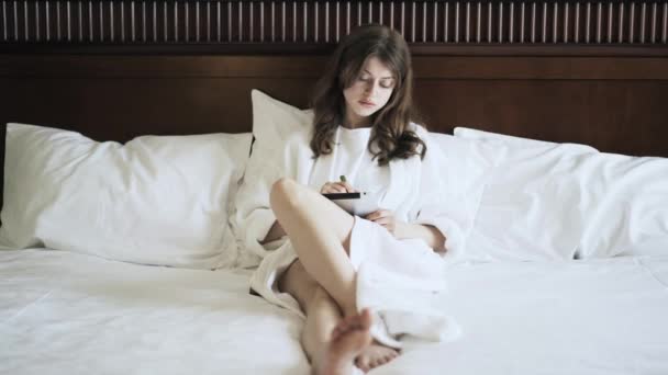 Young woman drawing on her tablet computer in bed, front view - Кадри, відео