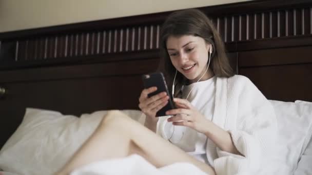 Young woman having a video call with her smartphone in bed - Metraje, vídeo