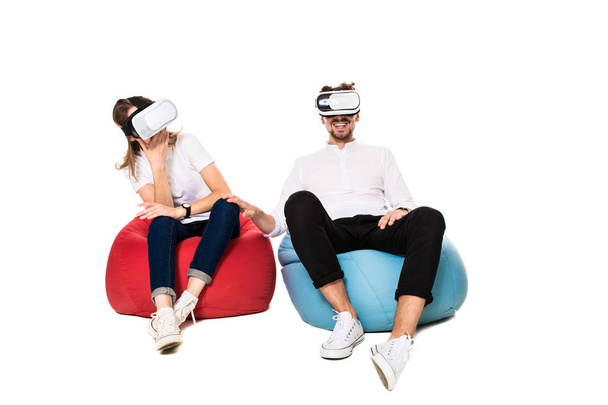 Eccitato giovane coppia sperimentando realtà virtuale seduto su beanbags isolato su sfondo bianco
 - Foto, immagini