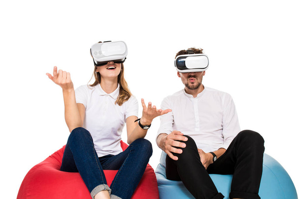 Eccitato giovane coppia sperimentando realtà virtuale seduto su beanbags isolato su sfondo bianco
 - Foto, immagini