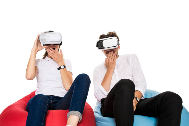 Захоплена молода пара відчуває віртуальну реальність, сидячи на мішках ізольовані на білому тлі
 - Фото, зображення