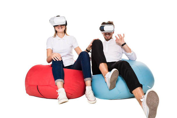 Excited young couple experiencing virtual reality seated on beanbags isolated on white background - Φωτογραφία, εικόνα