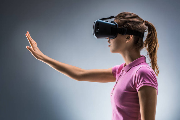 Jonge vrouw dragen VR headset in studio. Emoties. Zijaanzicht - Foto, afbeelding