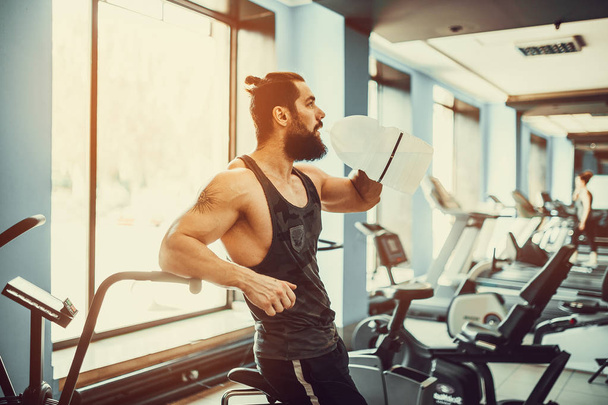 guy relaxing after workout and hold or drink water from big bottle in gym - Photo, Image