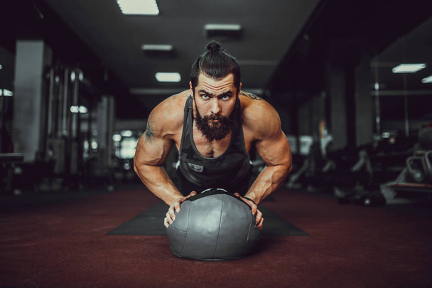 Muscled bearded man doing push ups from ball in gym. - Zdjęcie, obraz