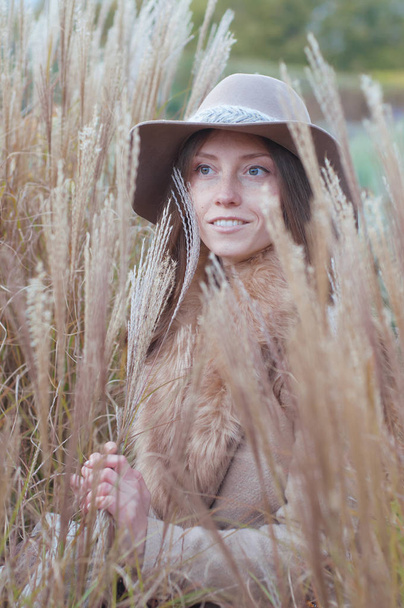 Vrouw in beige bontjas in het droge herfst veld - Foto, afbeelding